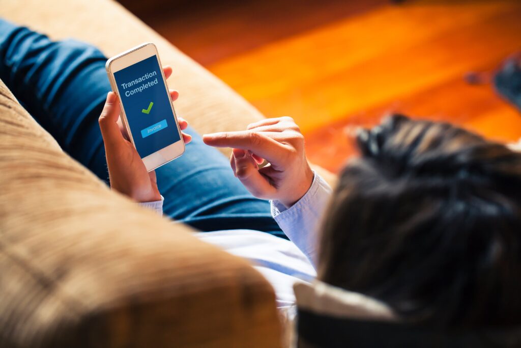 Woman using on line banking on mobile phone at home laying on the sofa.